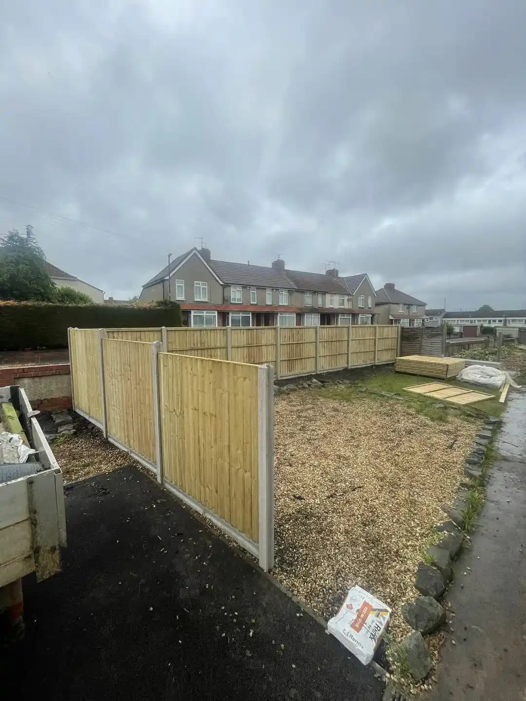 Closeboard fence with concrete posts enclosing a gravel front garden and side access area.