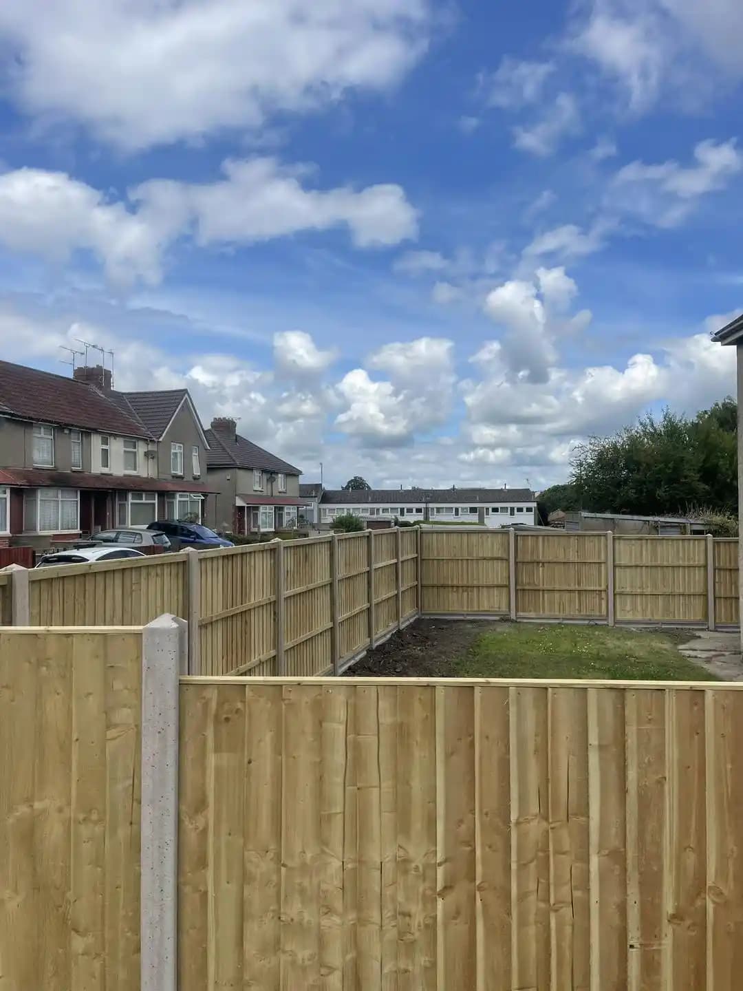 Closeboard timber fence panels with concrete posts enclosing a front garden under a bright blue sky.