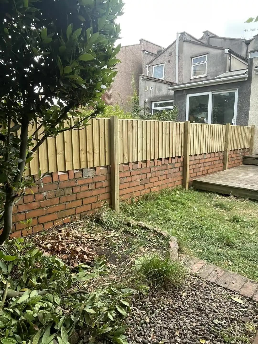 Closeboard timber fencing installed above a brick wall beside decking and garden planting.