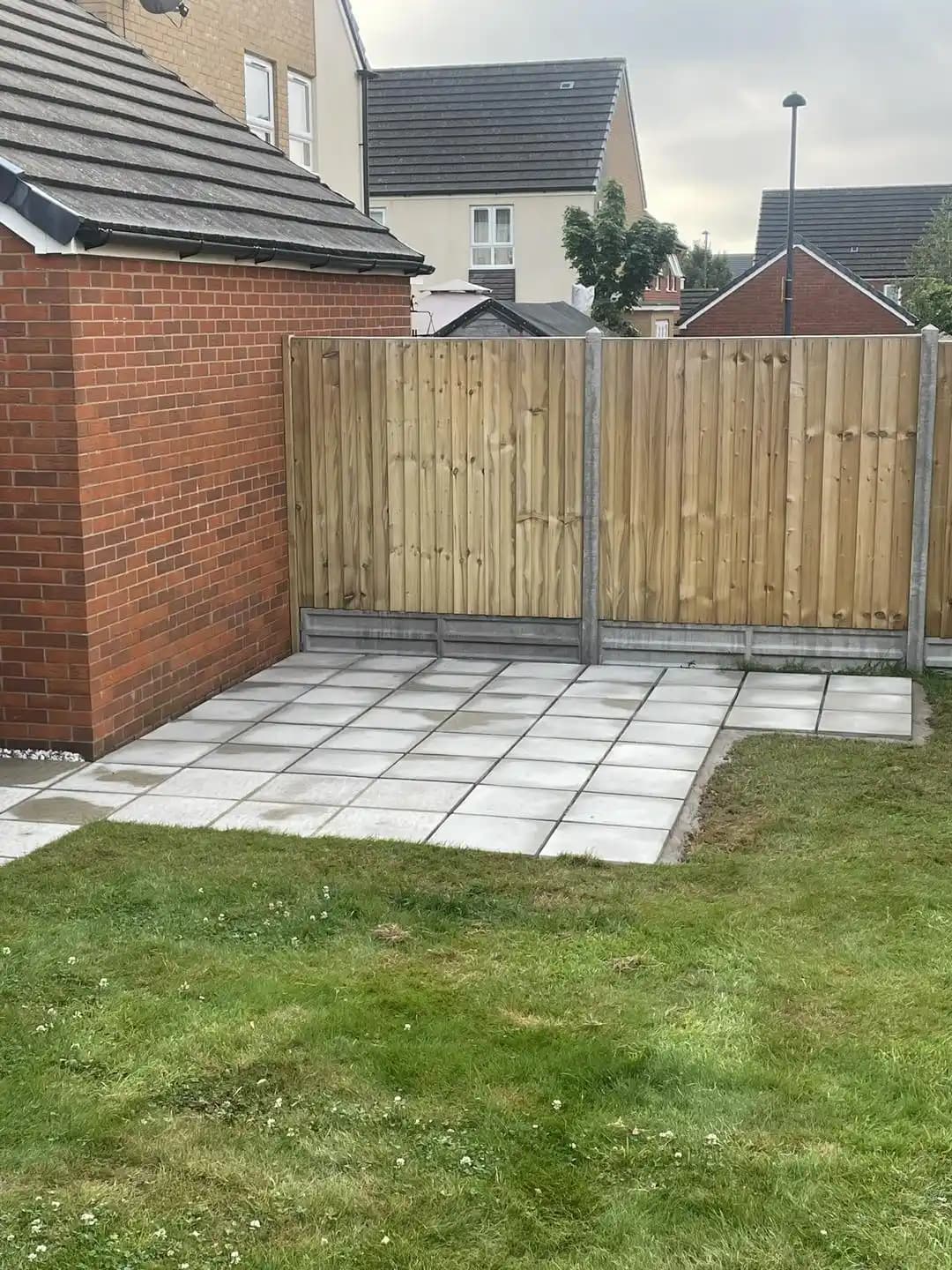 Closeboard fencing with concrete posts installed around a paved garden corner and lawn area.