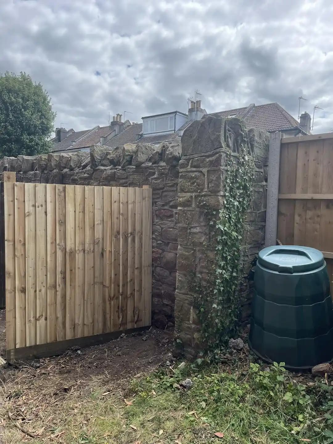 Closeboard timber garden gate installed beside an old stone wall and water butt in a rear garden.