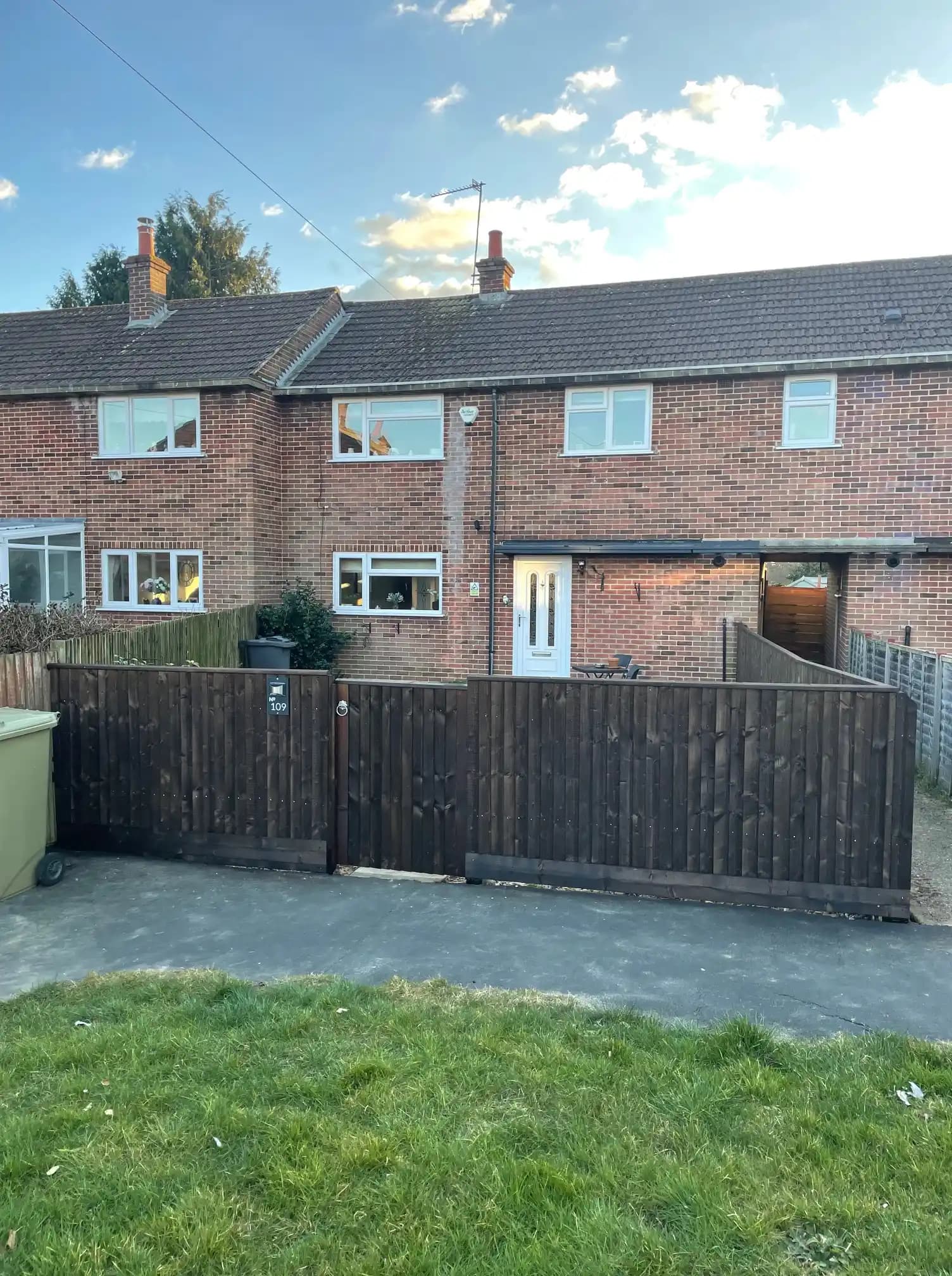 Dark stained timber front garden fence and gate outside a brick house, viewed from the street.