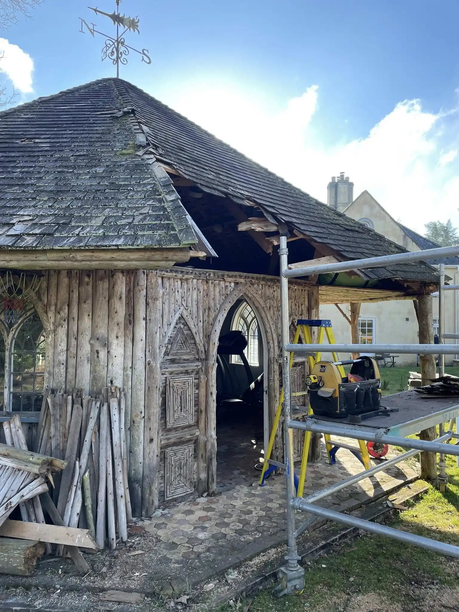 Close view of a timber outbuilding roof opening with scaffold and tools during specialist garden structure repair.