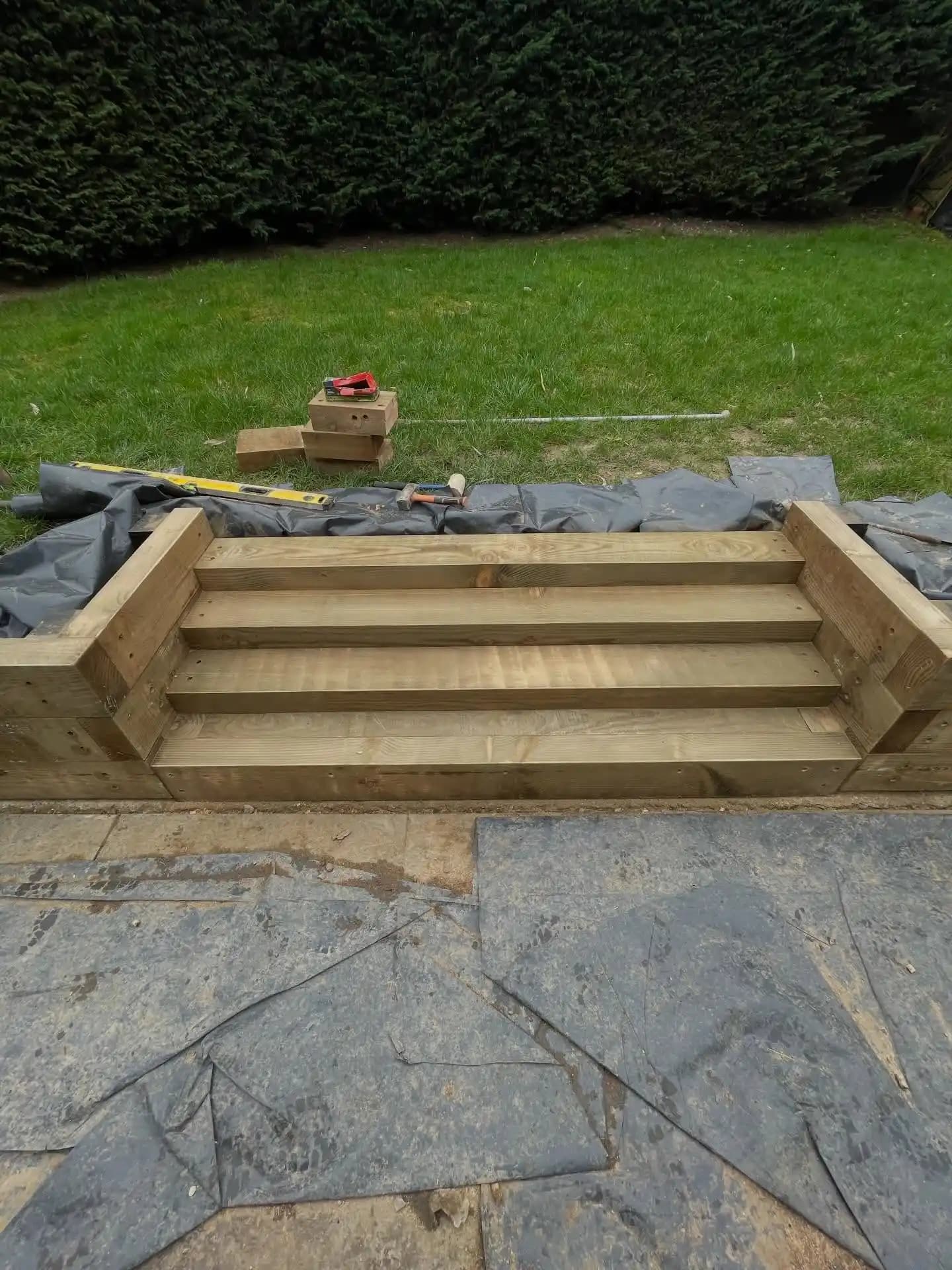 Completed timber sleeper steps with warm stained retaining wall and grey porcelain paving for a landscaped garden.