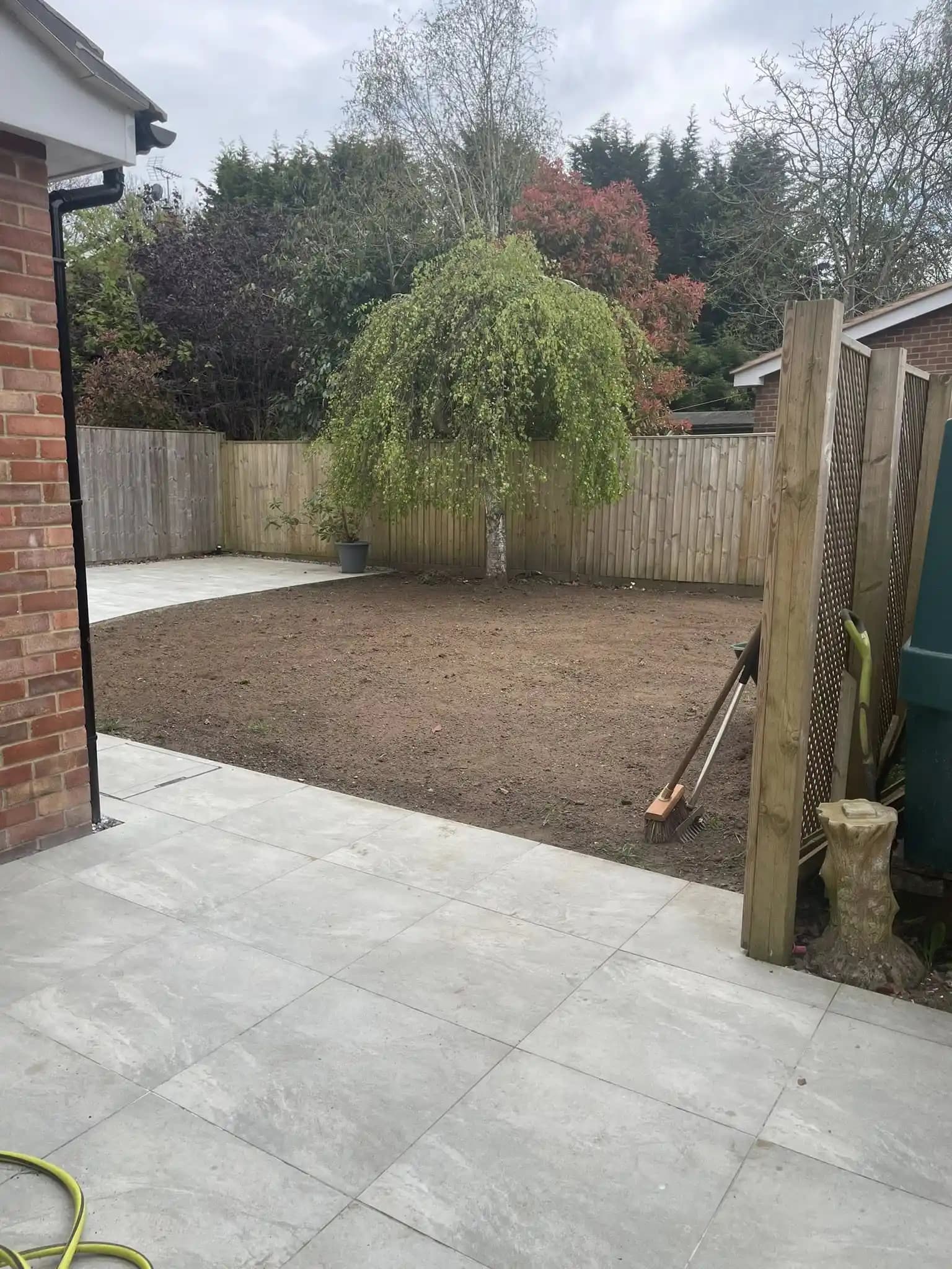 Freshly laid lawn with light porcelain patio paving, seating area and timber fencing after garden landscaping.