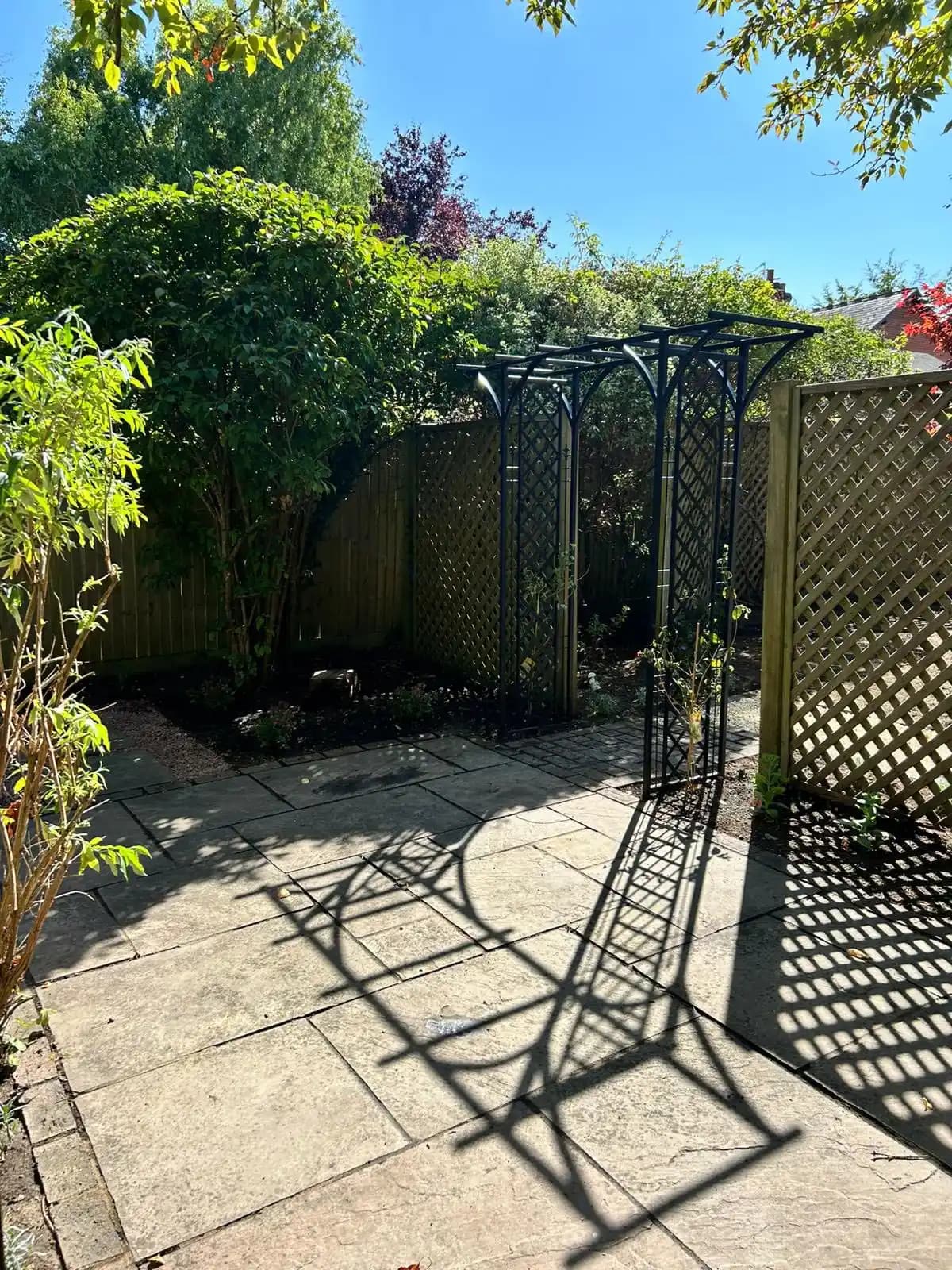 Curved white gravel path leading through trellis screens beneath a red acer tree in a newly landscaped garden.
