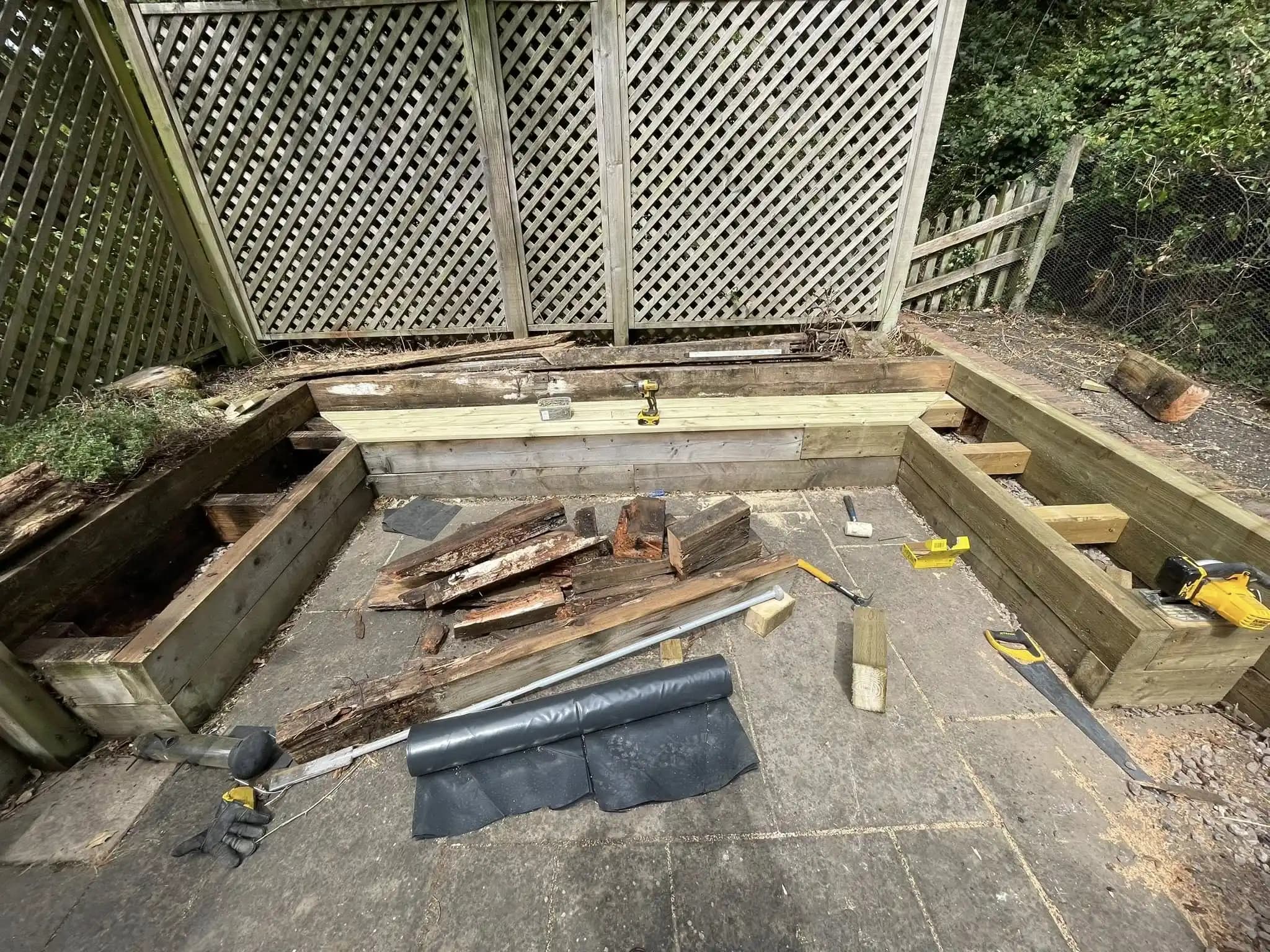 Pergola entrance with raised timber beds, red gravel seating area and planted borders in a landscaped garden.