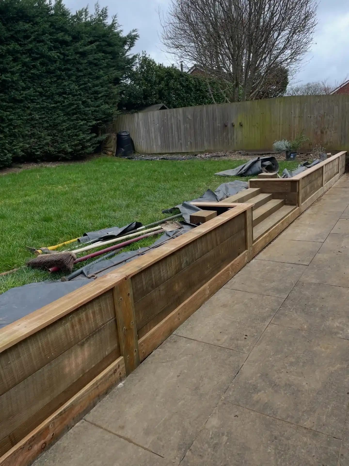 Finished grey porcelain patio with timber sleeper retaining wall, steps, decorative gravel and lawn seating area.