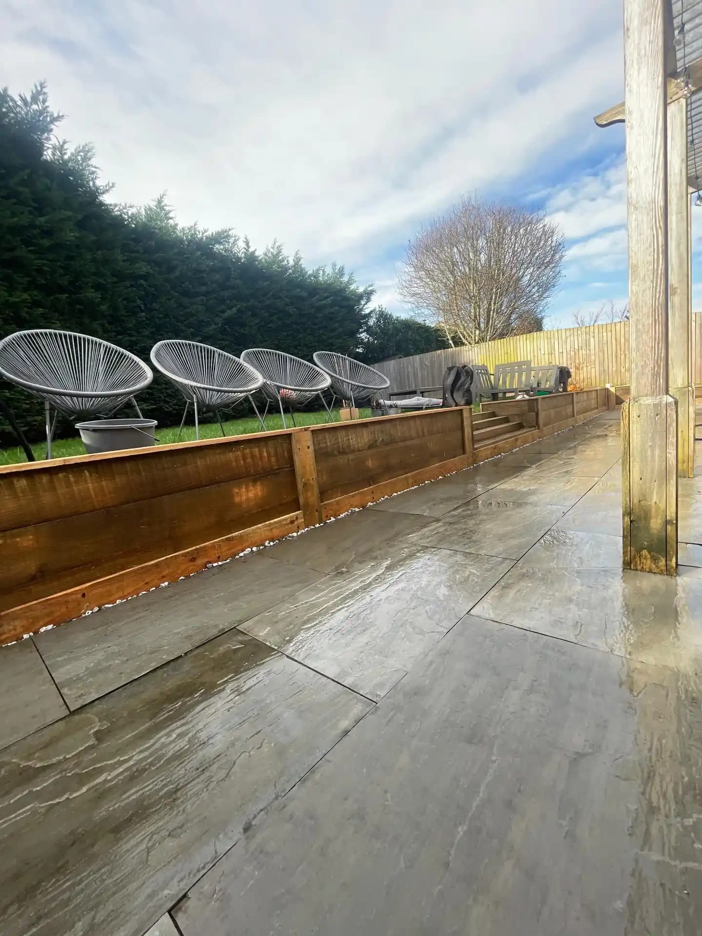 Spacious grey porcelain patio with timber sleeper edging, raised lawn, pergola posts and garden seating area.