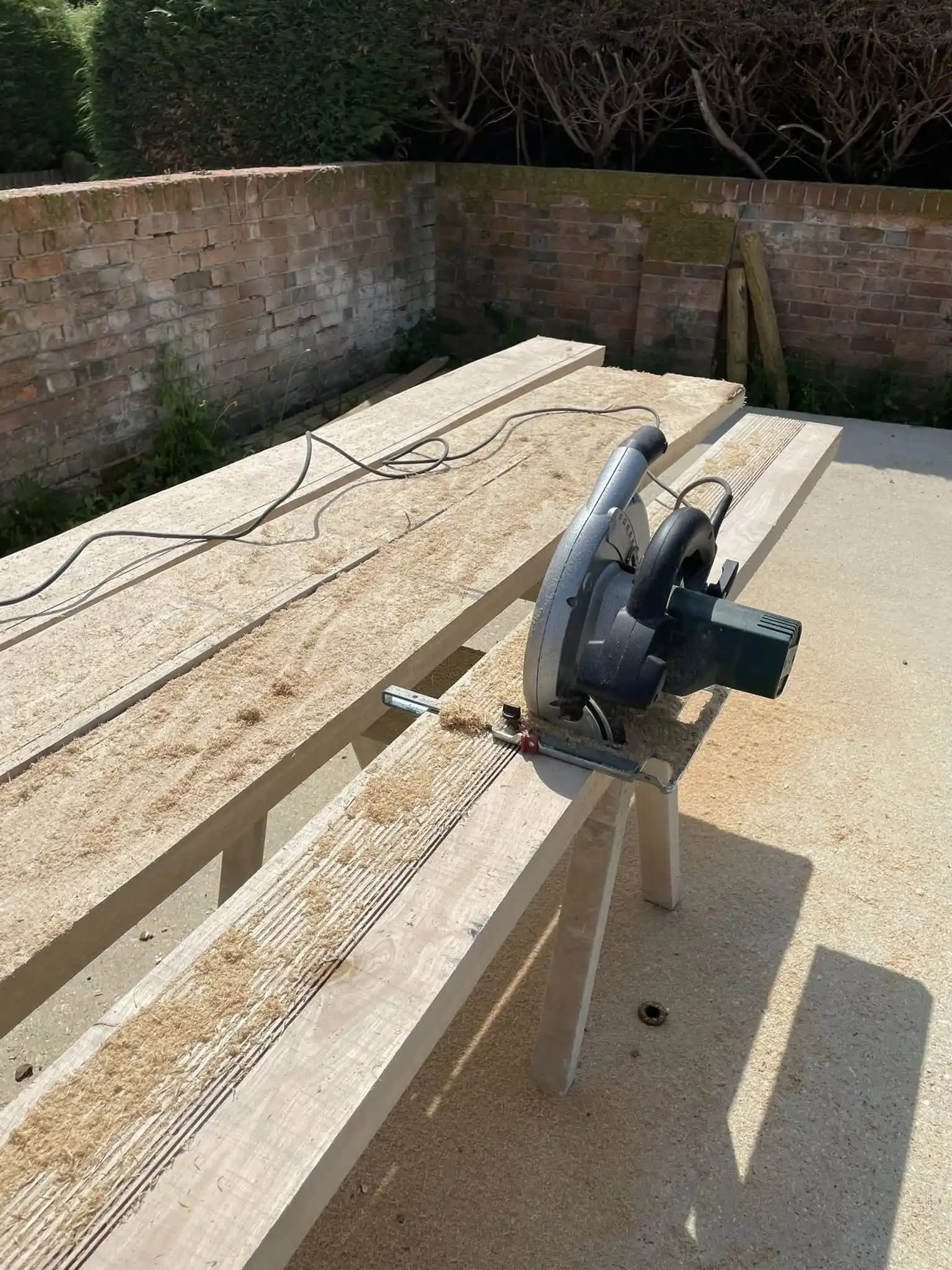 New long timber sleeper raised bed installed along a garden boundary with mature planting and fencing.