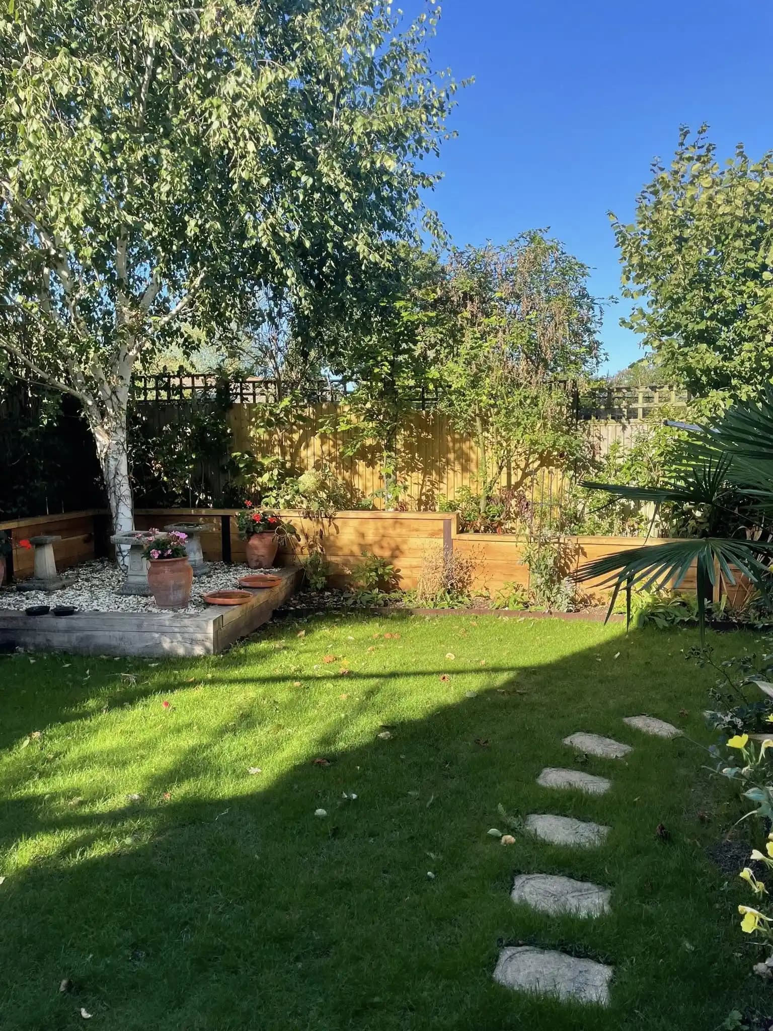Sunny garden with fresh lawn, sleeper raised beds, planted borders and stepping stones after landscaping work.