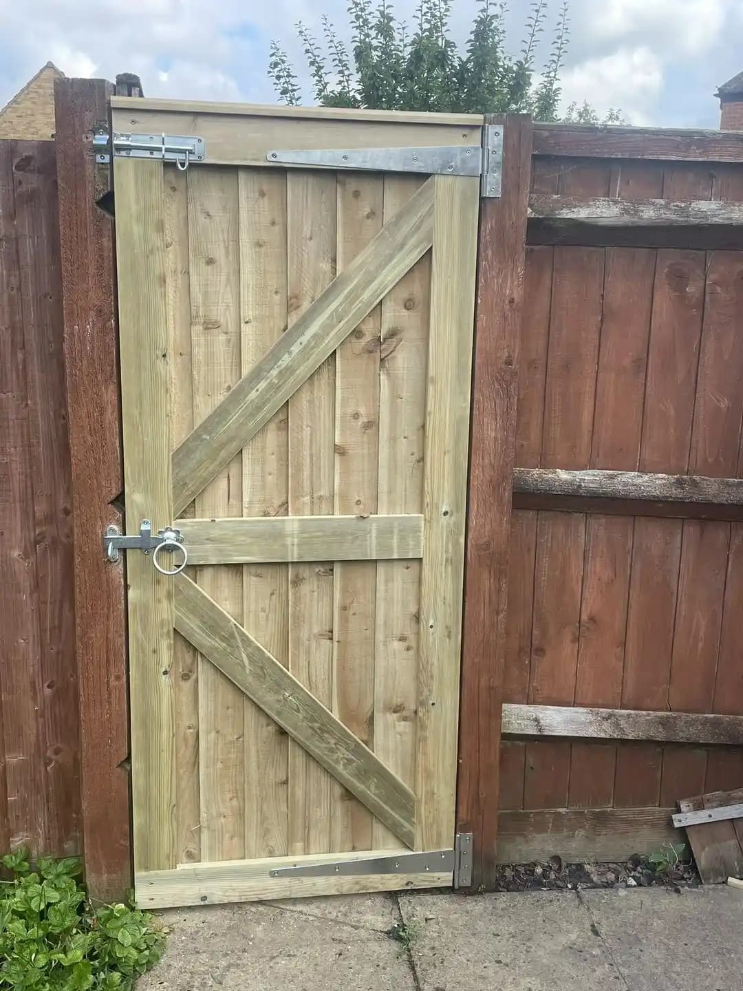 Framed ledged and braced timber gate with galvanised hinges and latch fitted between existing fence panels.