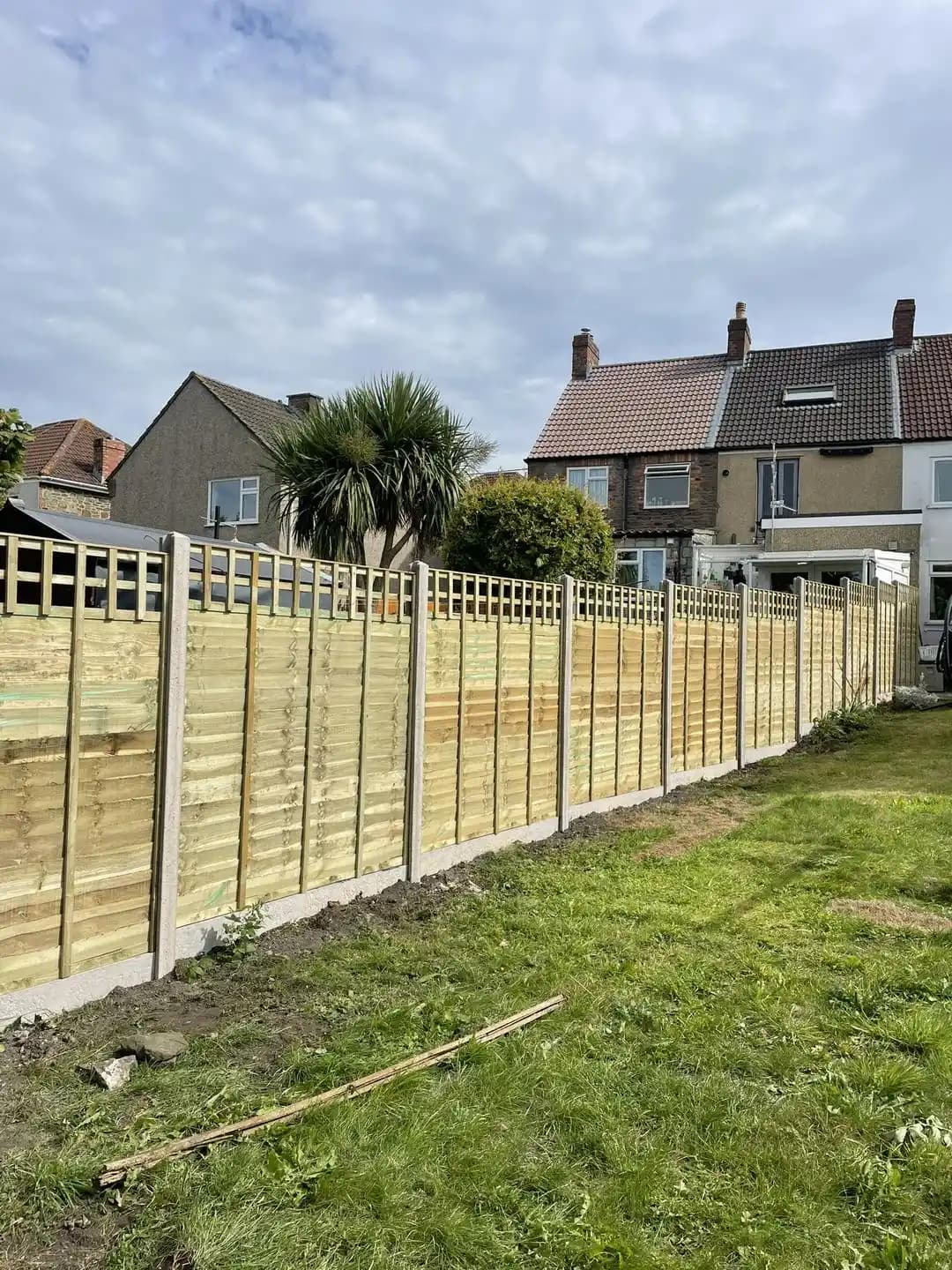 Long run of closeboard fencing with concrete posts and trellis top installed beside a lawn.