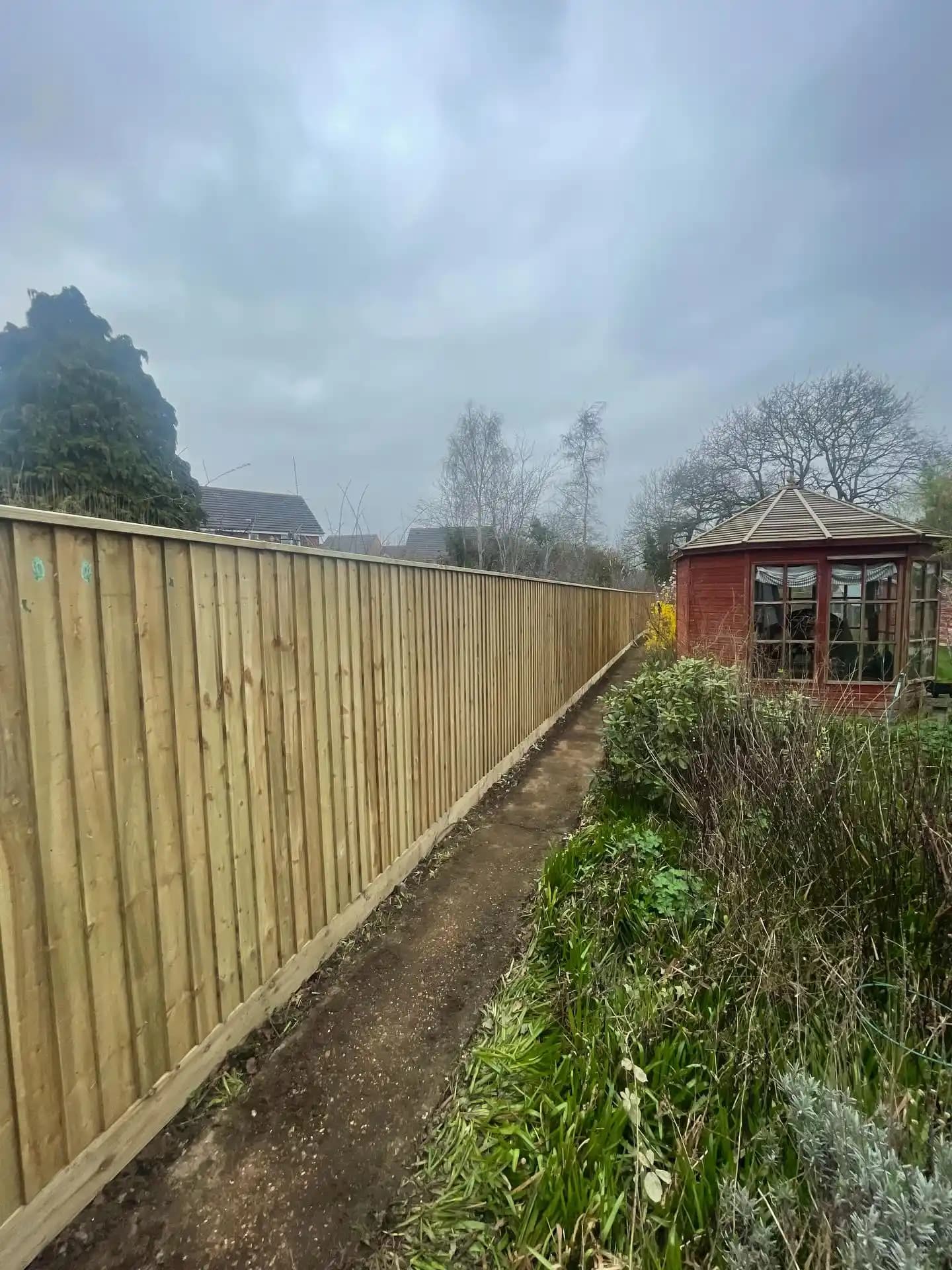 Long new closeboard garden fence with capping running beside a path and planted border in a garden.