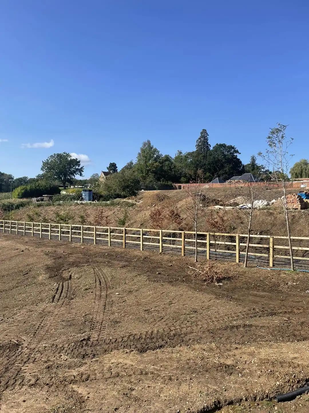 Long stretch of post and rail timber fencing installed along a cleared development site.
