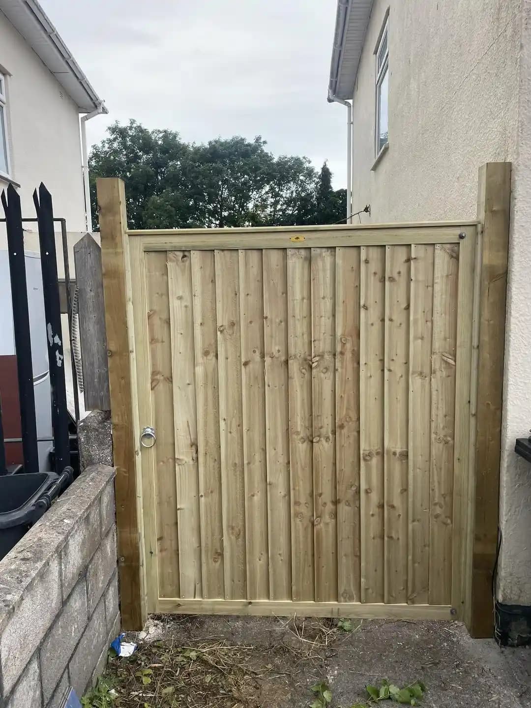 New solid timber side gate with ring latch installed between houses for secure garden access.