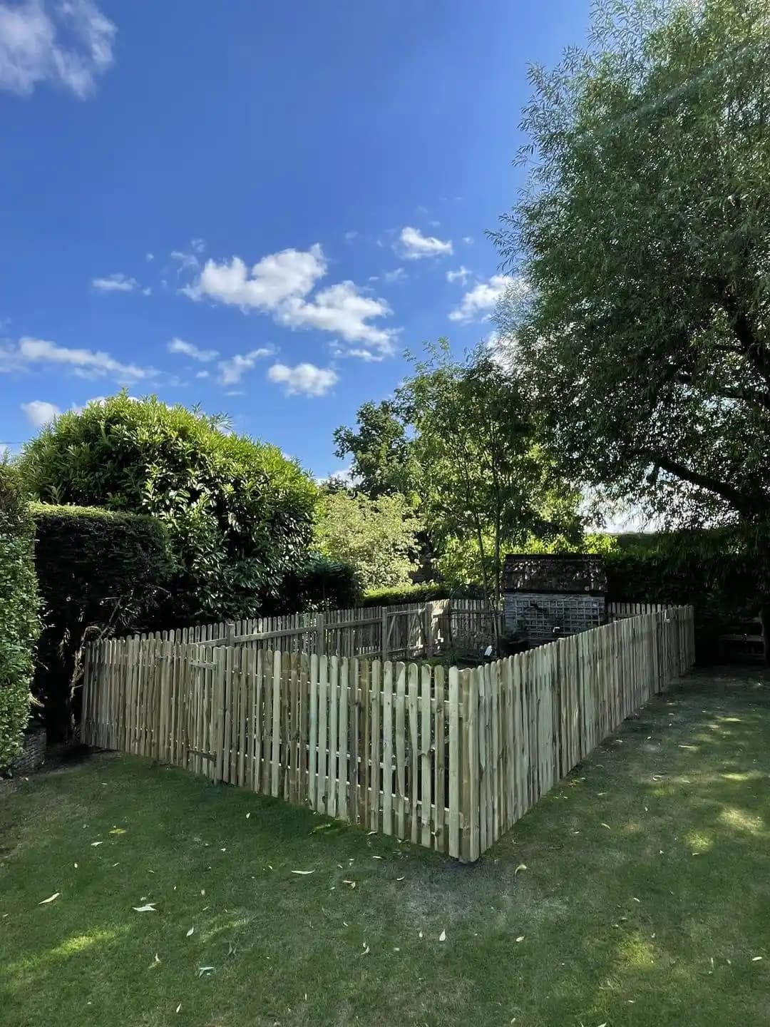 Timber picket fence enclosing a small garden area beneath mature trees.