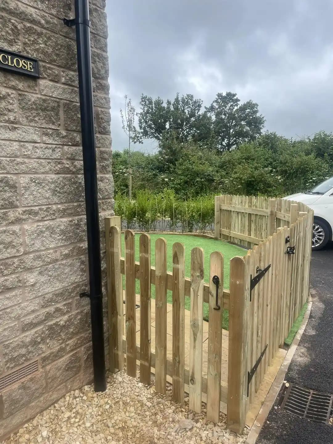 Timber picket fence and matching gate enclosing a small artificial lawn beside a house.