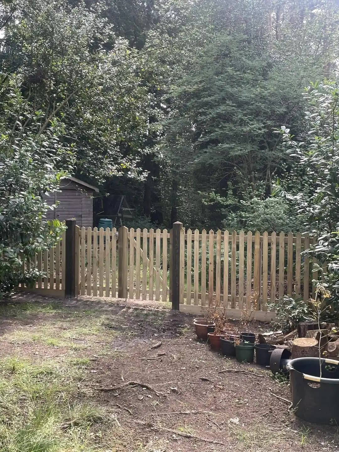 New timber picket fence and matching gate enclosing a shaded wooded garden area.