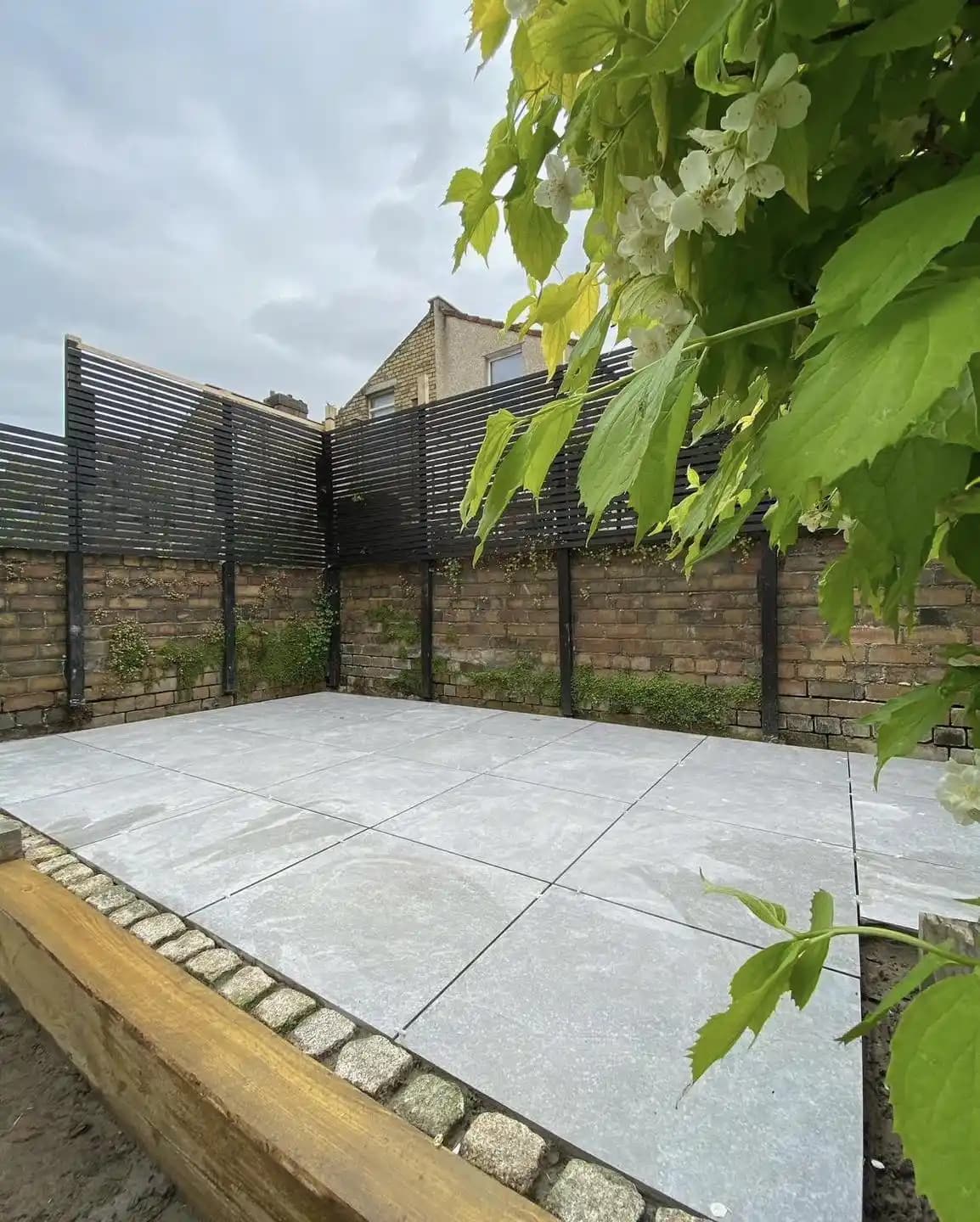Light grey porcelain patio with a black slatted privacy screen installed above a brick garden wall.
