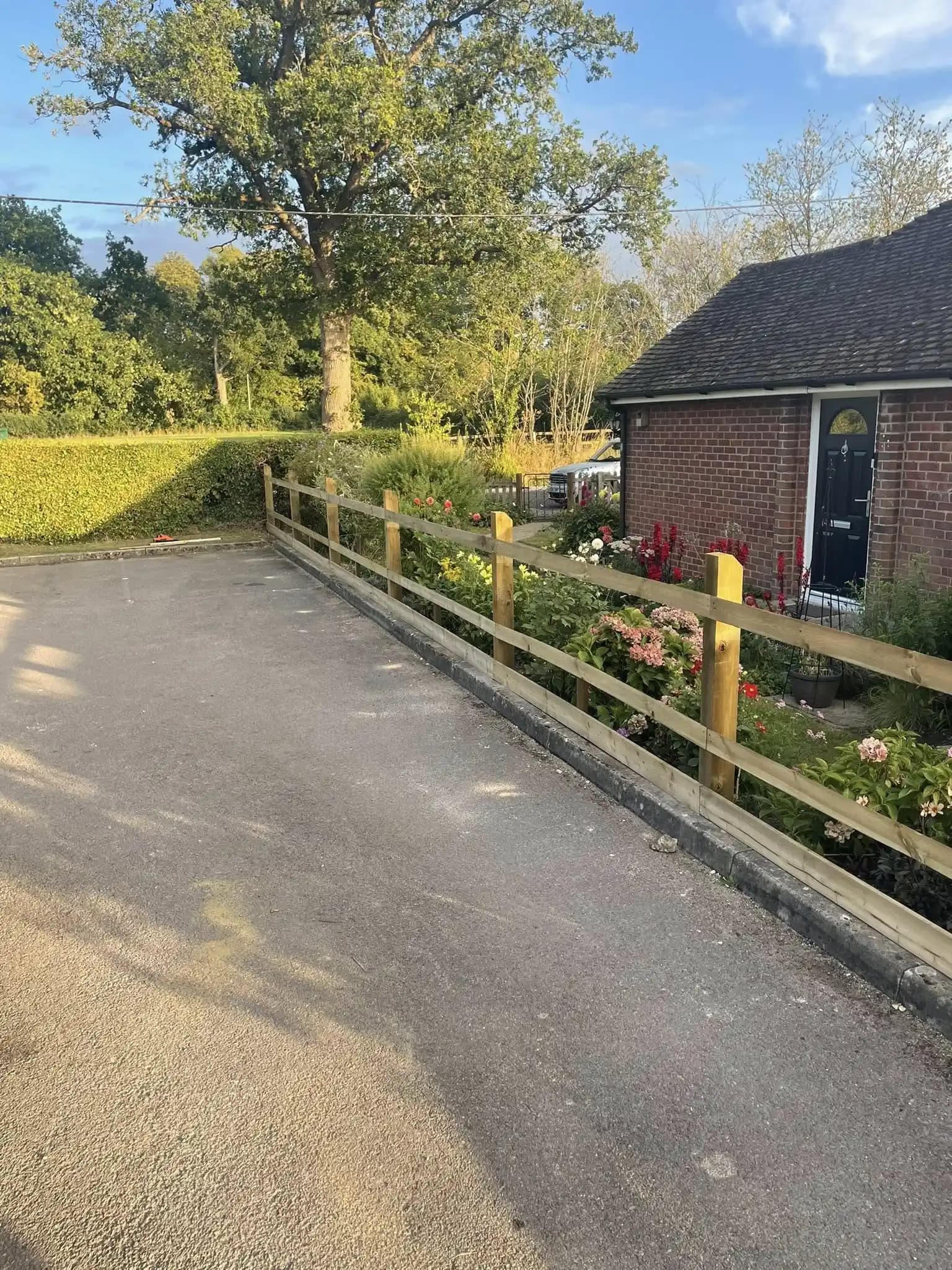 New timber post and rail fence installed beside a driveway and front garden planting.