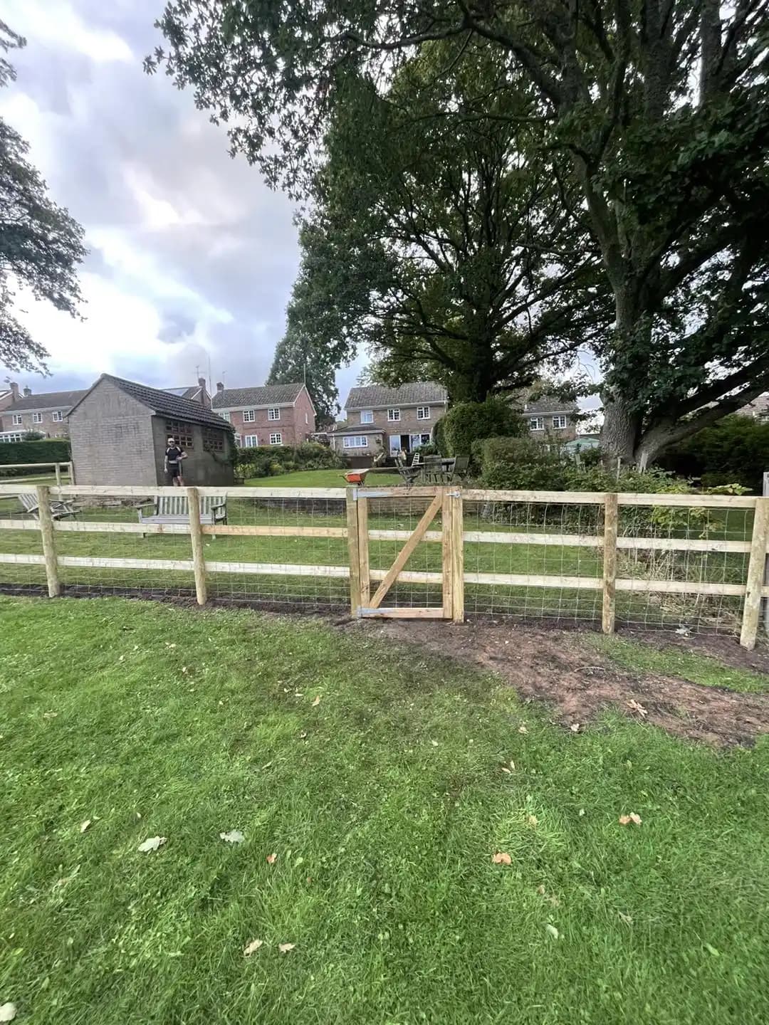 Post and rail timber fence with wire mesh and a matching pedestrian gate installed across a lawn.