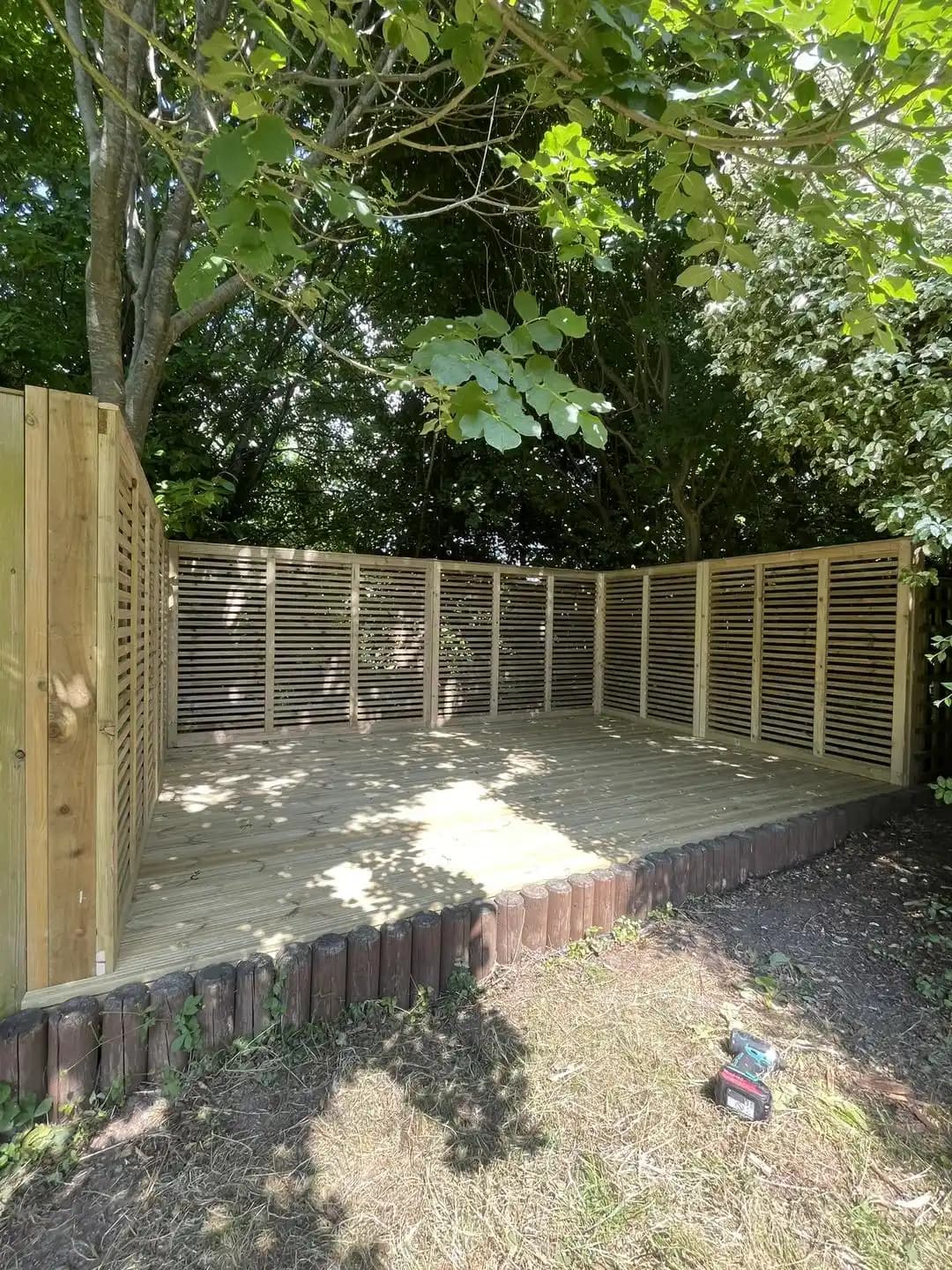 Raised timber deck finished with horizontal slatted privacy screens in a shaded garden area.