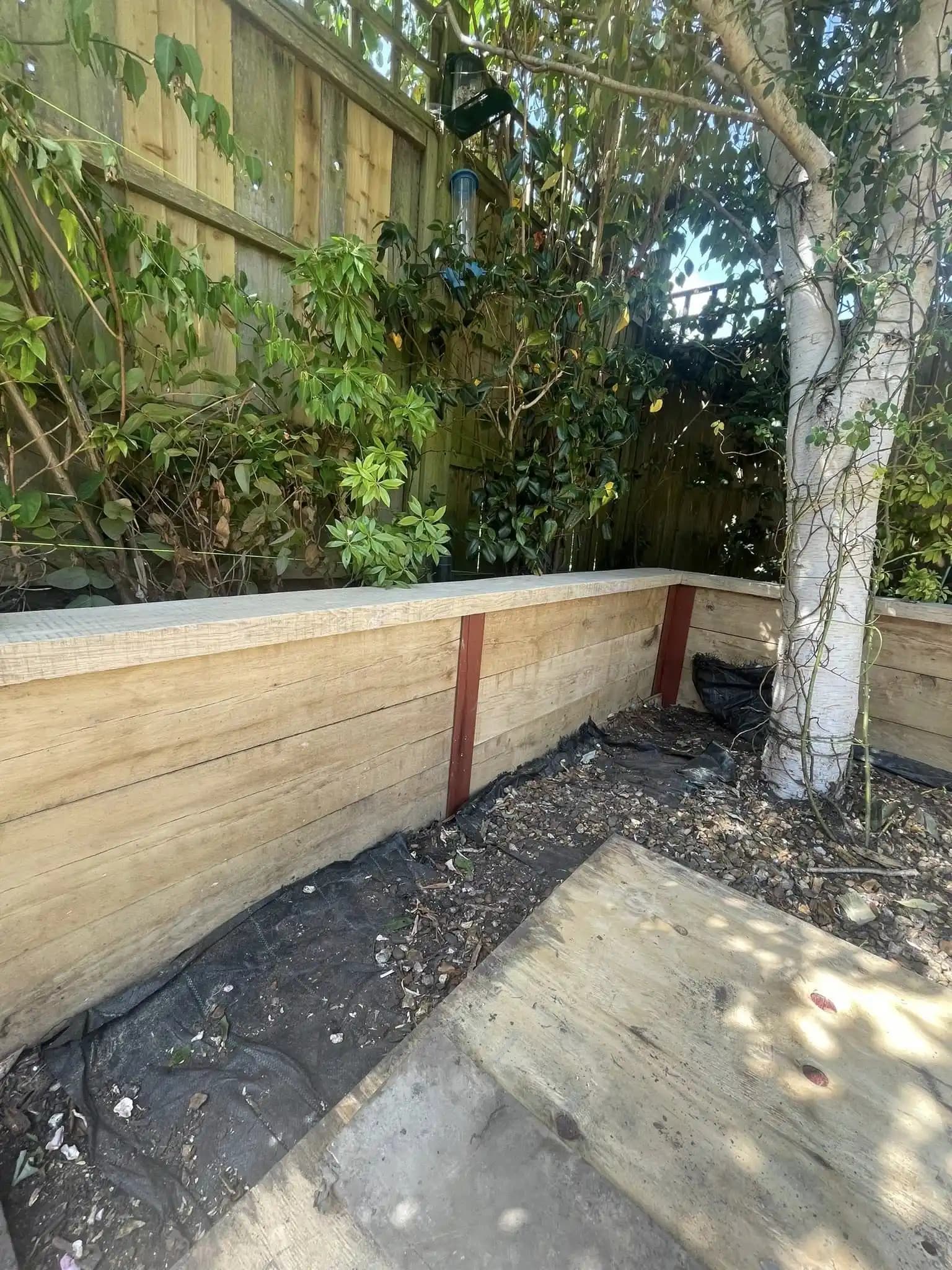 New timber sleeper retaining wall around a mature garden tree with membrane and prepared planting area.