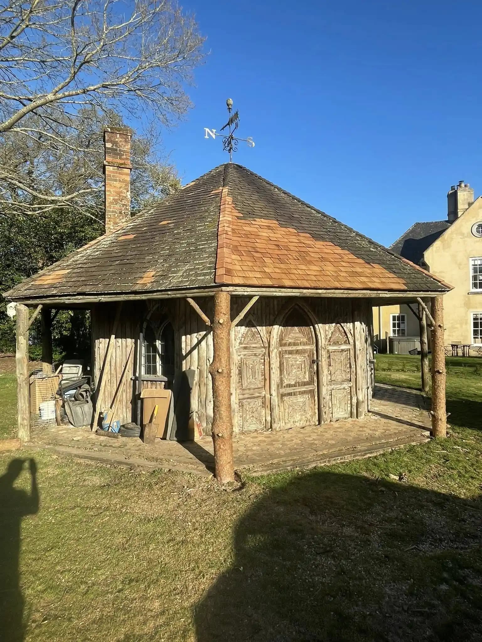 Rustic timber garden building with partial roof repair and new shingles under a clear blue sky.