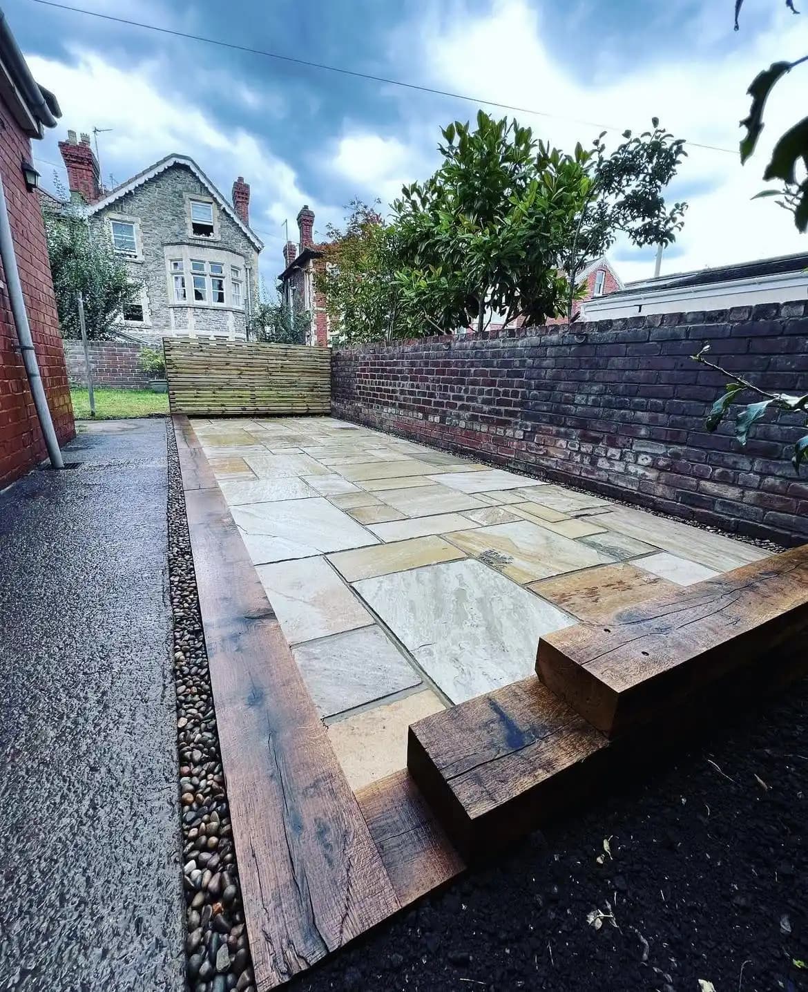New sandstone patio finished with timber sleeper edging and a gravel drainage strip.