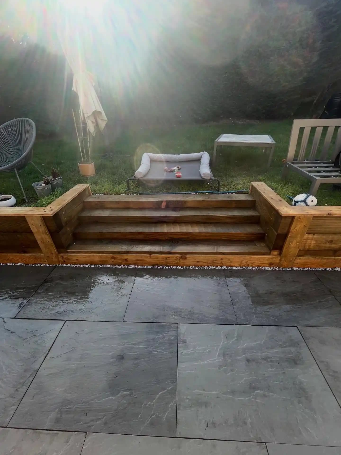 Garden sleeper retaining wall under construction with membrane and tools before finishing beside a patio and lawn.