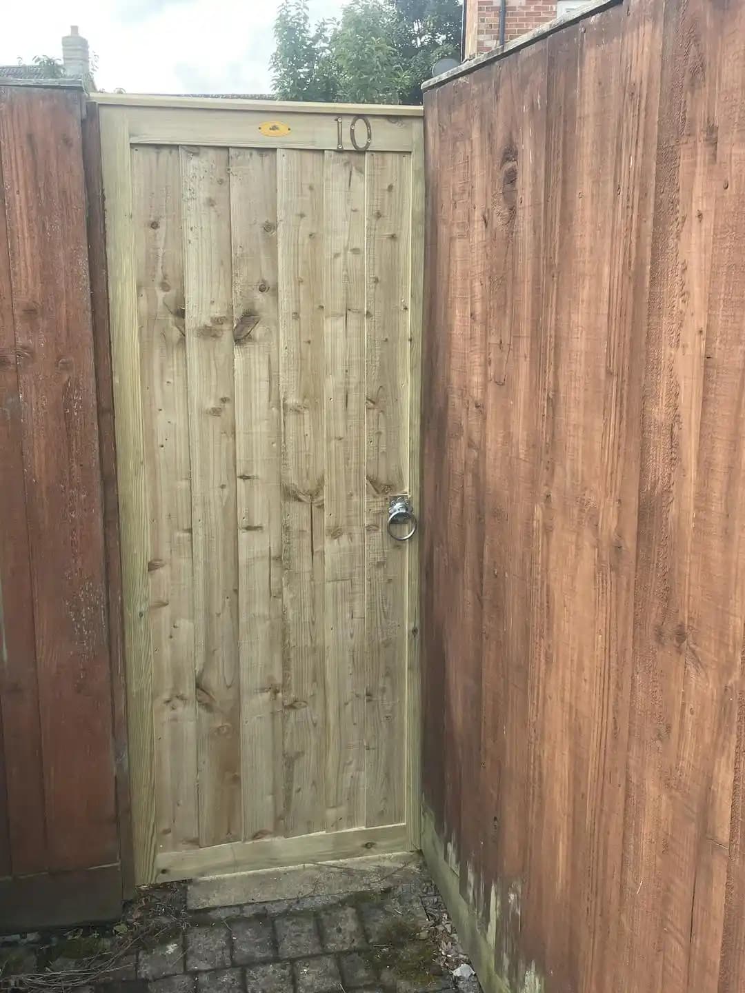 Tall solid timber side gate installed neatly between existing boundary fences with a ring latch.