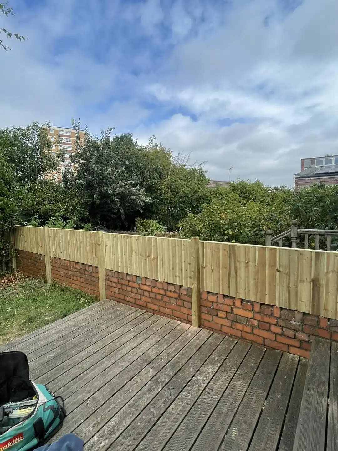 Vertical timber fence extension installed above a brick garden wall beside a raised deck.
