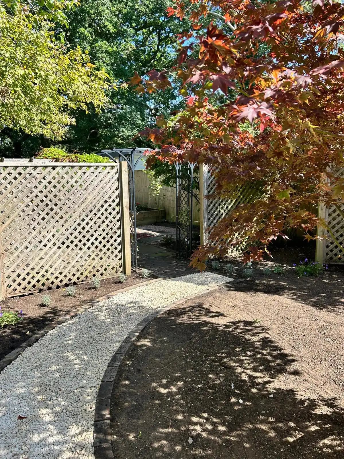 Timber pergola with raised beds, red gravel path and stepping stones forming a practical seating garden.