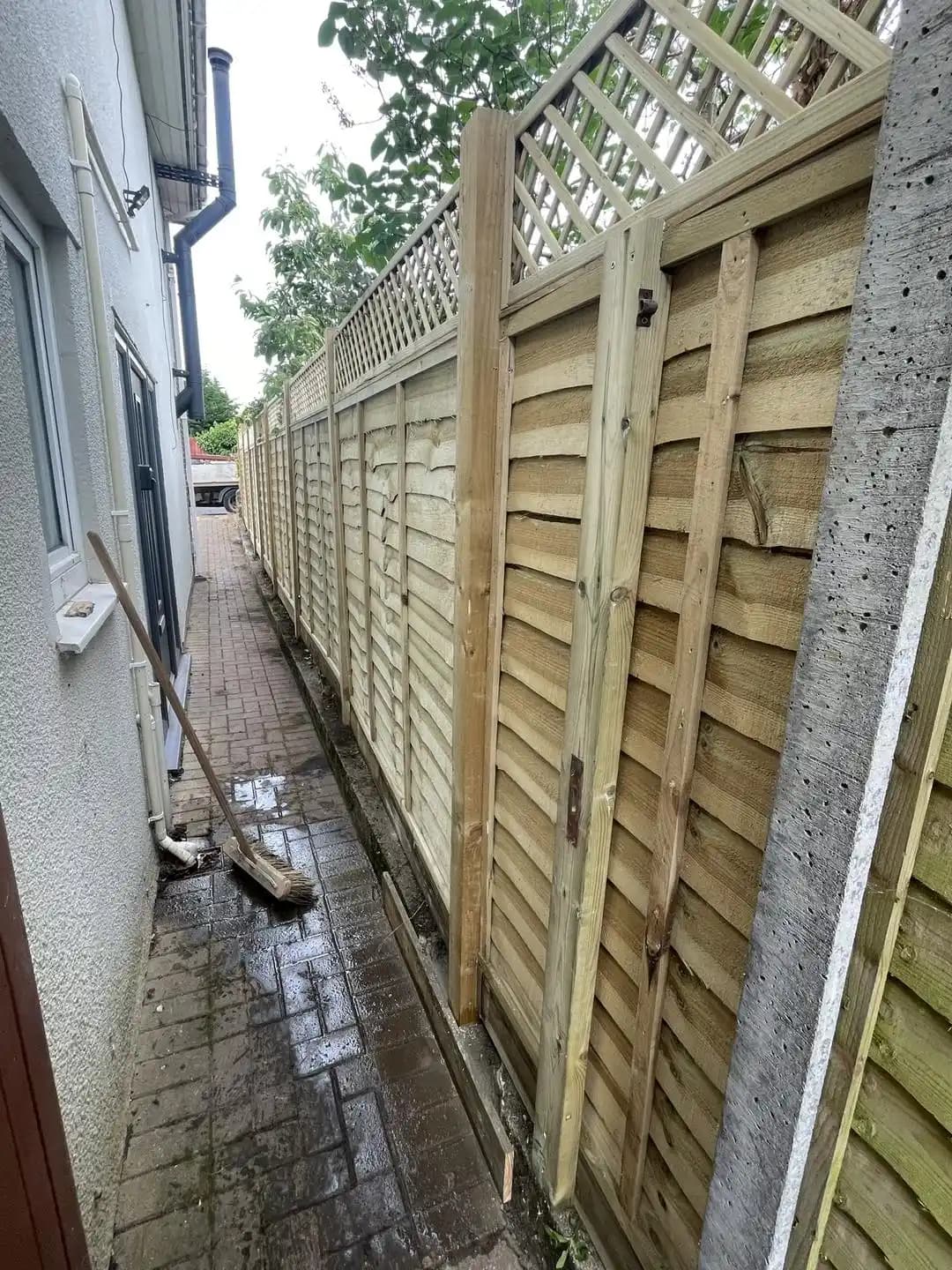 Closeboard fence panels with decorative lattice trellis installed along a narrow side path beside a house.