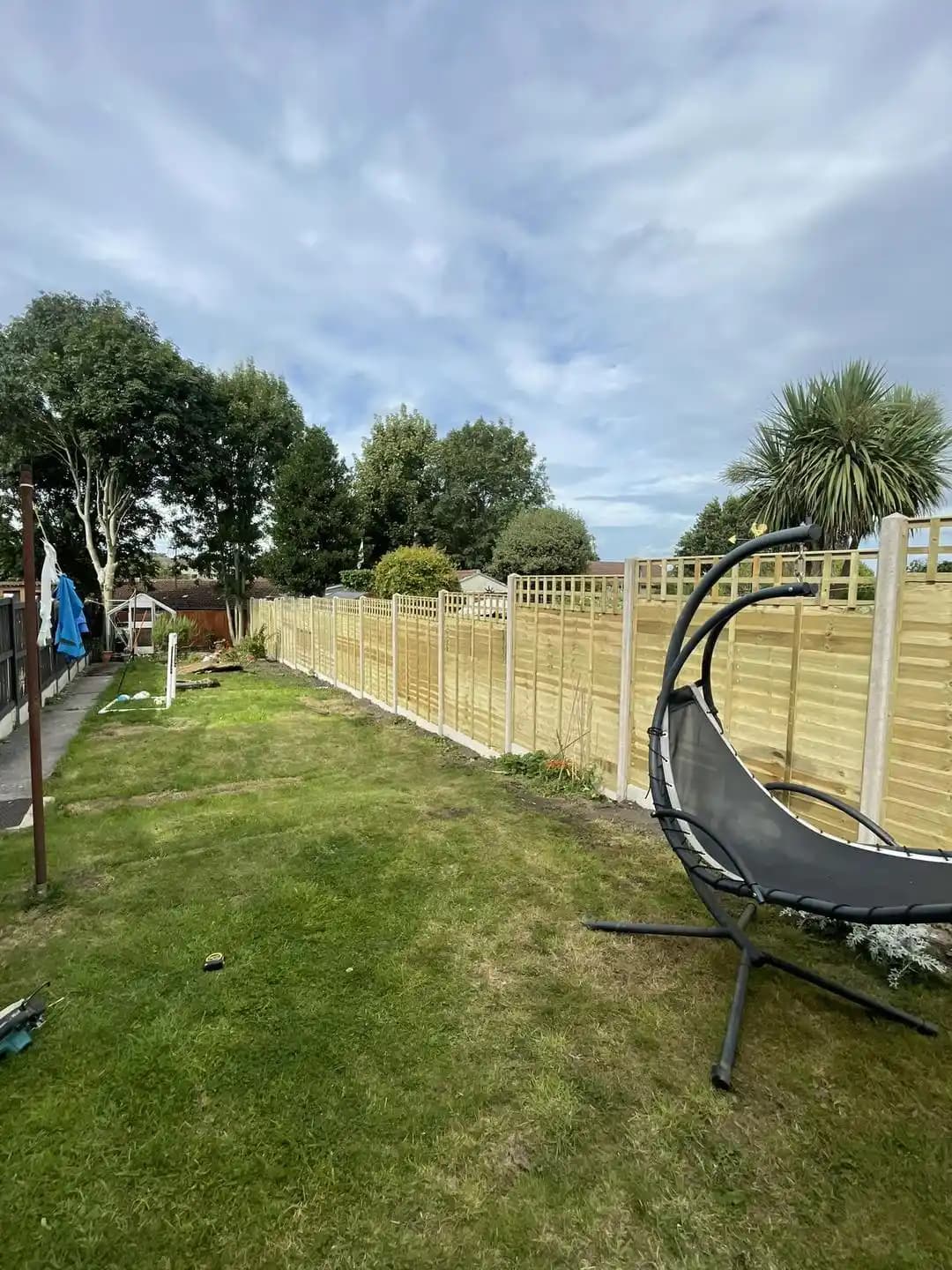 Long timber boundary fence with trellis top installed beside a lawn and garden seating area.
