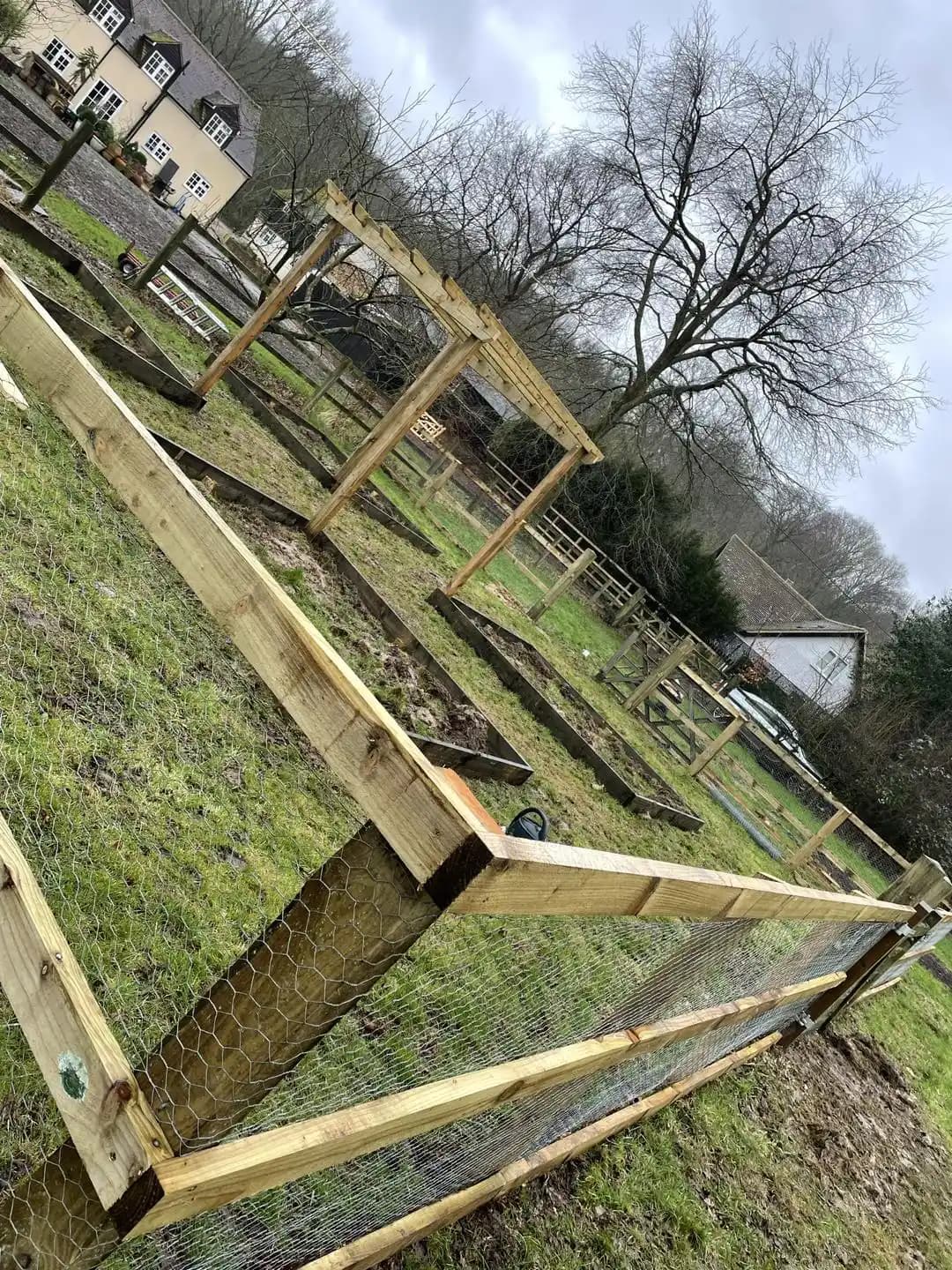 Timber post and rail fence with wire mesh surrounding vegetable beds and a garden pergola.